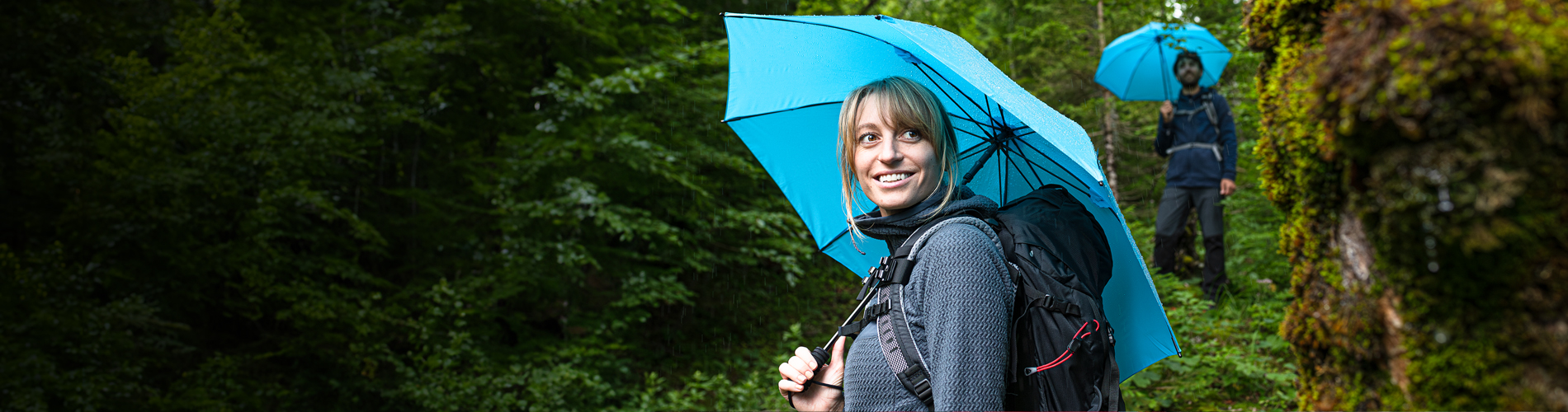 Wanderin mit hellblauem Trekking-Schirm und Rucksack im Wald
